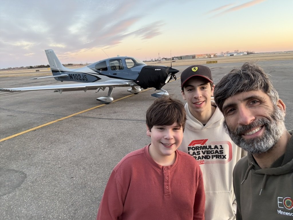 Daniel with Isaac and Jonah on the ramp in front of an airplane at sunset