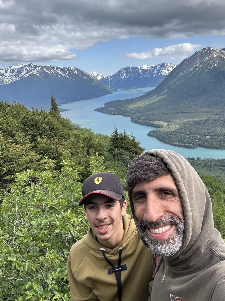 Daniel and his son on a hiking trail above a glacier-blue lake