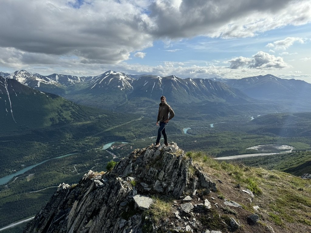 Daniel standing on a rocky mountain summit above a river valley